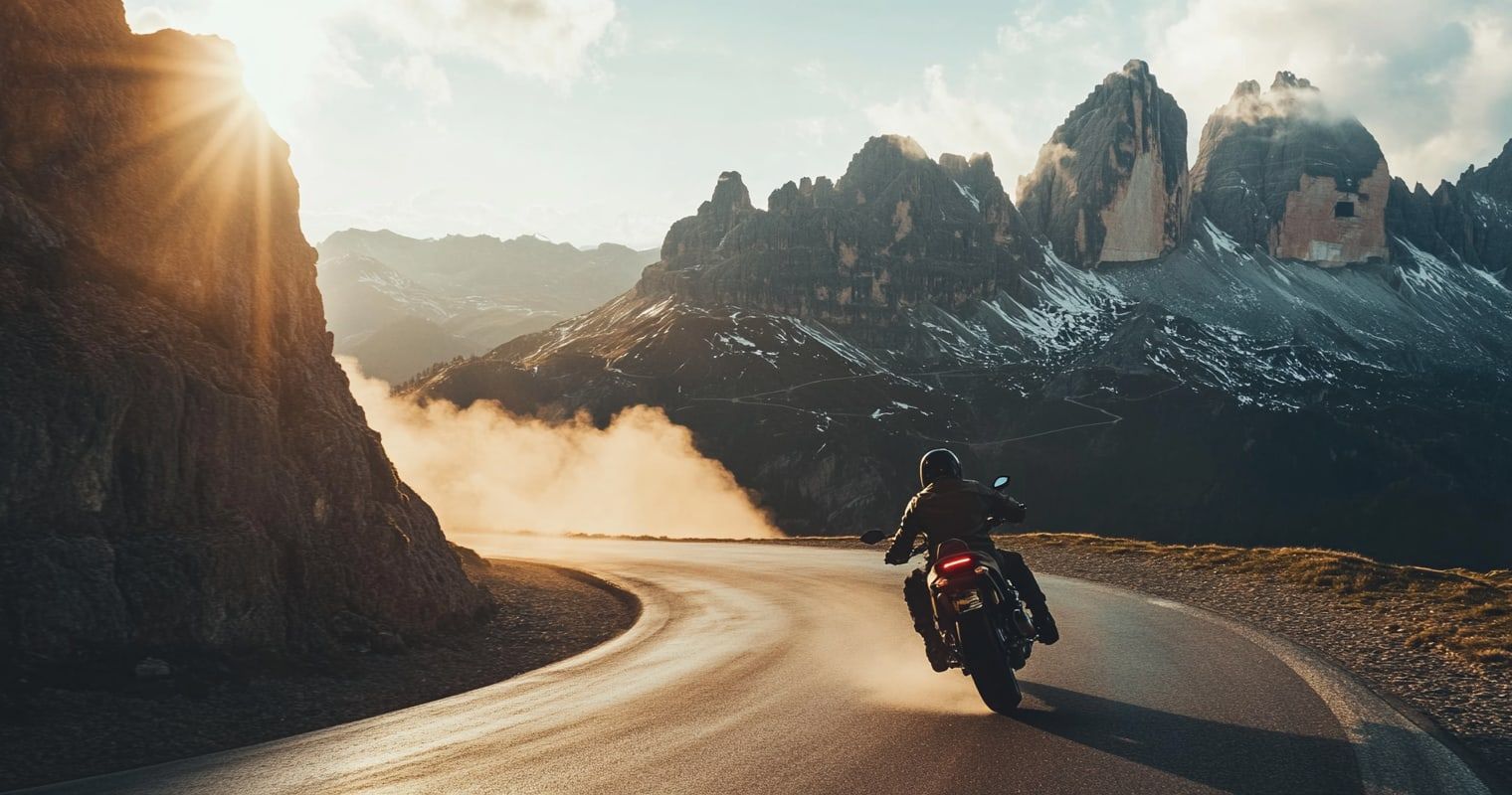 A motorcyclist leaning into a sweeping Dolomites bend, jagged peaks behind (illustrative)